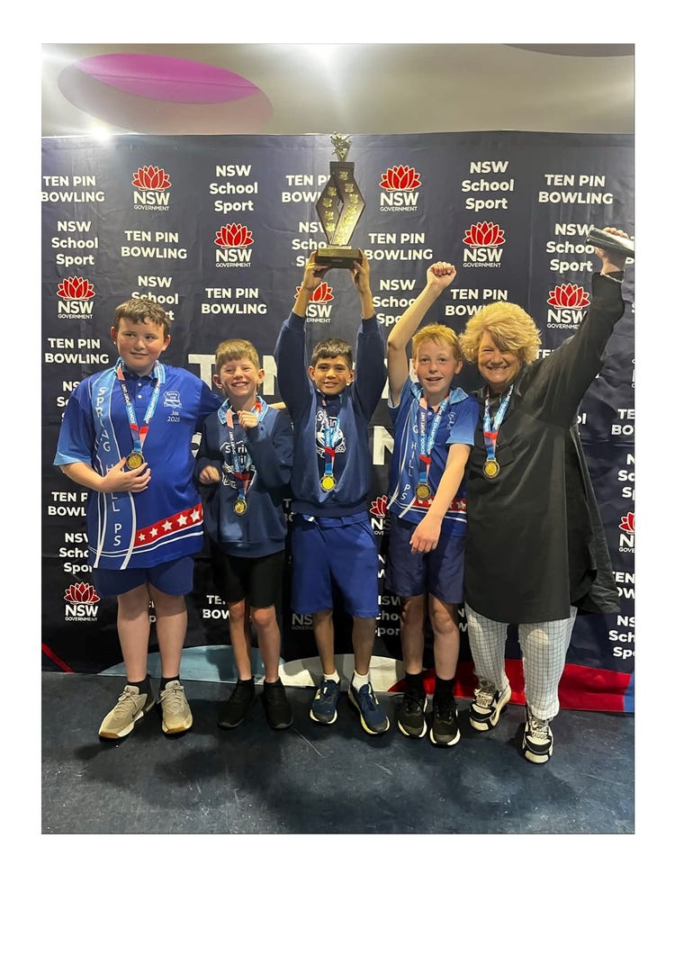A photo of four winning students and Mrs Mac standing next to them. There is a banner behind them saying NSW School Sport, Ten Pin Bowling. The students all have medals around their necks and the child in the middle of the photo is holding a large trophy above his head.