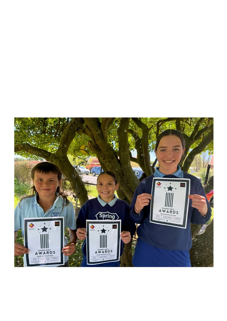 Three students standing holding certificates. One male and two female students. They all have smiles on their faces and large tree in the background.