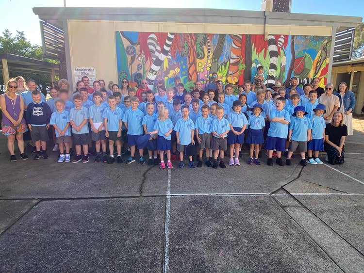 A full school photo including staff standing out the front of the admin building. There is a large painted mural in the background.
