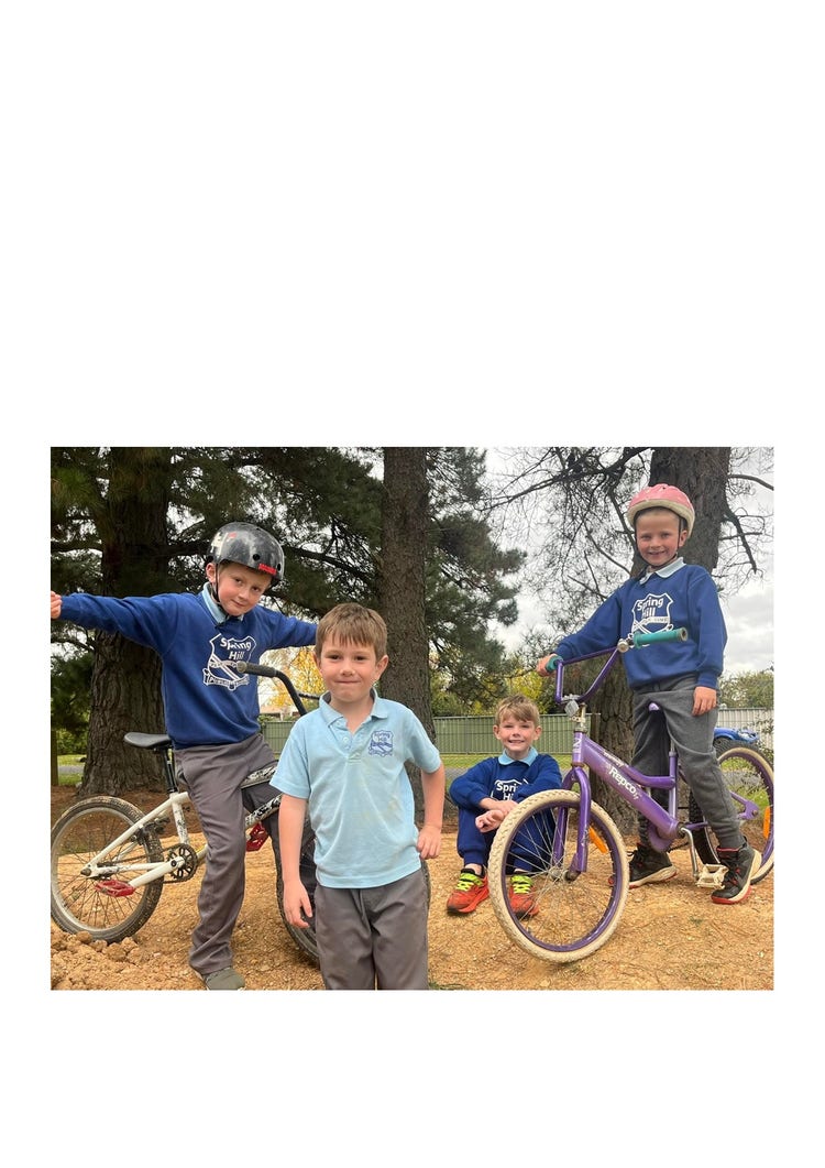 Four boys standing for a photo on the bike track. Two of the boys are sitting on their bikes with helmets on ready to ride.