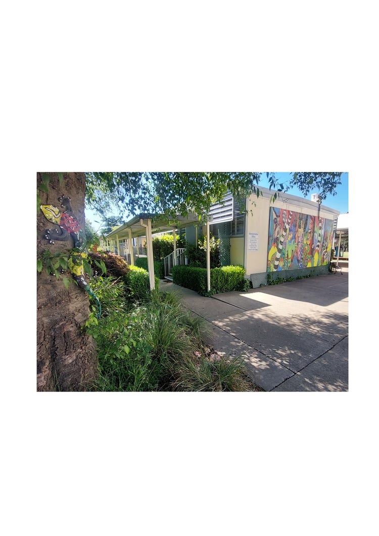 A photo of the office admin building. The side wall has a large brightly painted mural on the wall and there is an undercover walkway going along the front of the building.